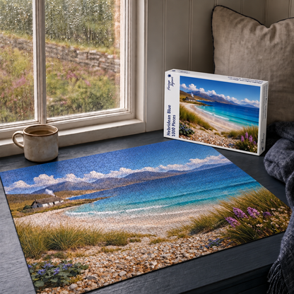Hebridean Blue 1000 piece jigsaw box and completed puzzle on a window seat, showing a white croft cottage above a turquoise Hebridean bay with marram grass and sea thrift